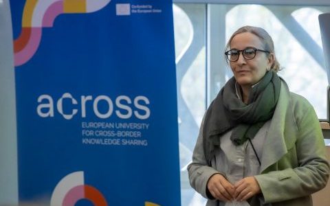 Uczestnik wykładów w ramach Dni Rumuńskich na Politechnice Białostockiej przed plakatem Across