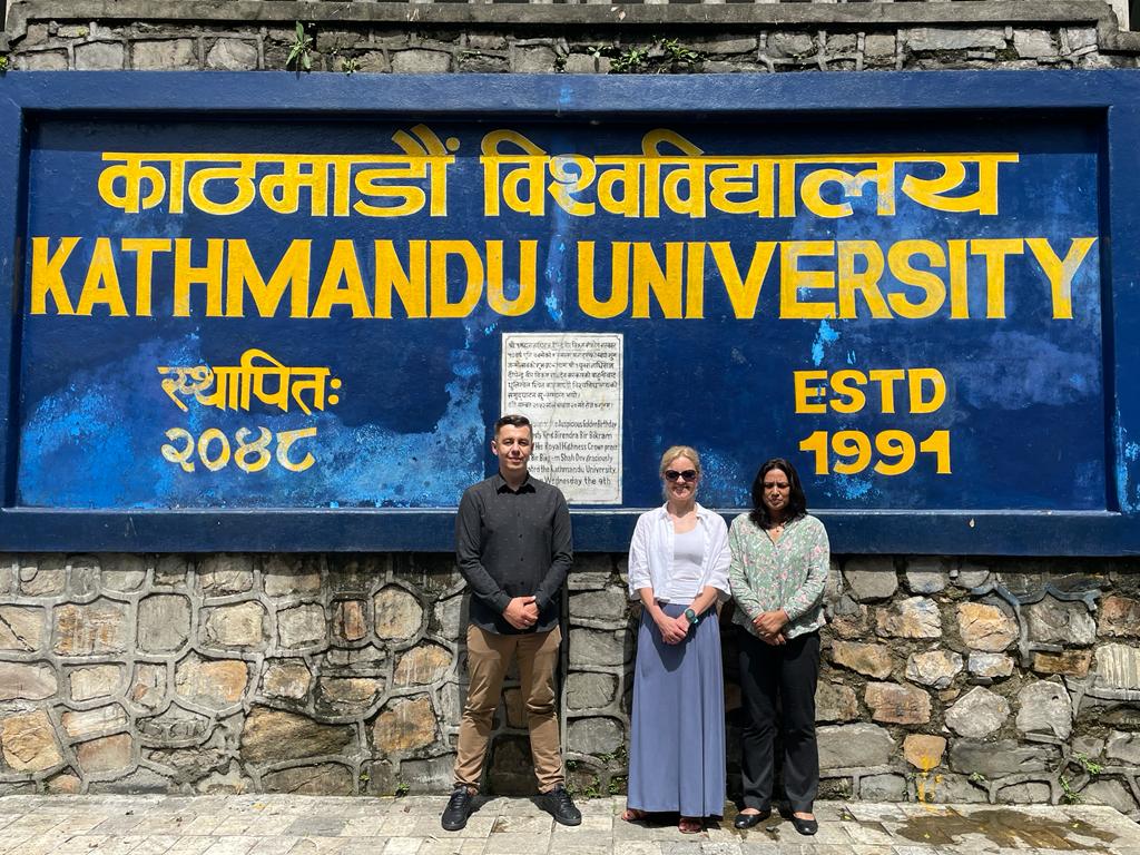 Katarzyna Kochaniak i Artur Mazur z Politechniki Białostockiej, oraz Jyoti Pradhan z Uniwersytetu Kathmandu na tle tablicy z napisem Uniwersytet Kathmandu