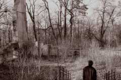 A-man-walking-through-a-cemetery-with-a-clock-tower-in-the-background