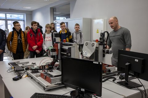 grupa uczniów przygląda się maszynom obsługiwanym przez wykładowcę