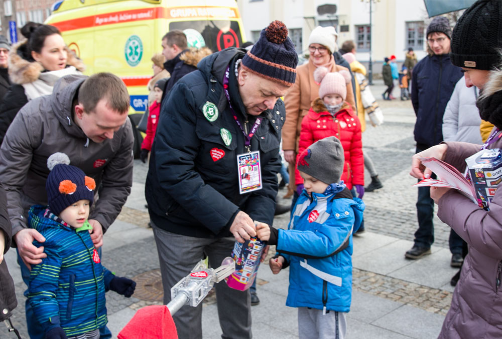 rektor Politechniki Biąłostockiej pomaga dziecku we wrzuceniu datku do puszki WOŚP. Puszka jest umieszczona w uchwycie na wysięgniku łazika marsjańskiego. Kwesta w ramach 28. Finału WOŚP odbywała się na Rynku Kościuszki w Białymstoku