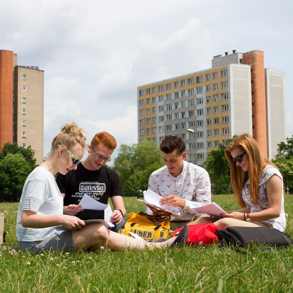 studenci siedzący na trawie przed akademikami PB