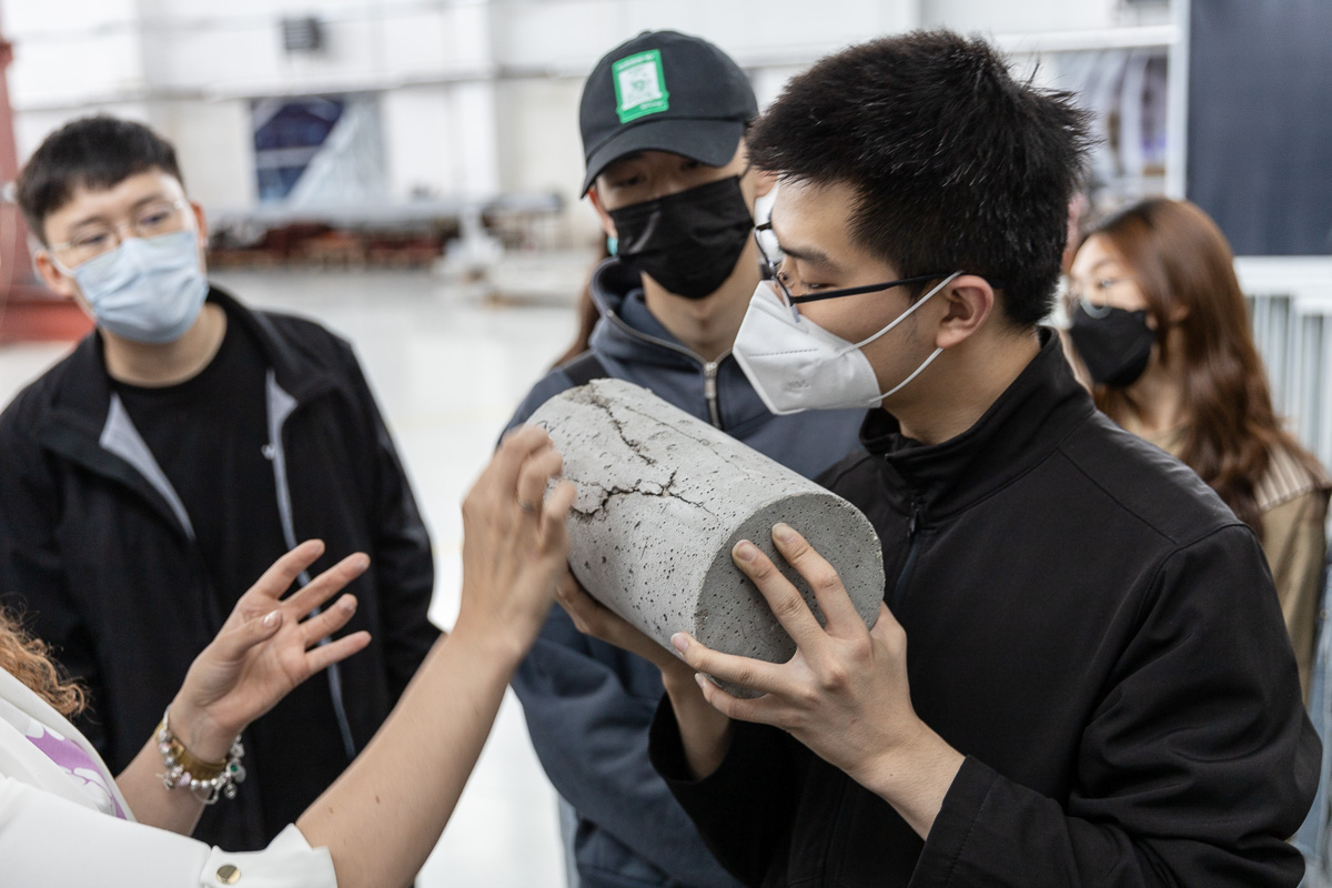 chińscy studenci patrzą na próbkę betonu poddaną badaniom wytrzymałościowym (ściskanie)