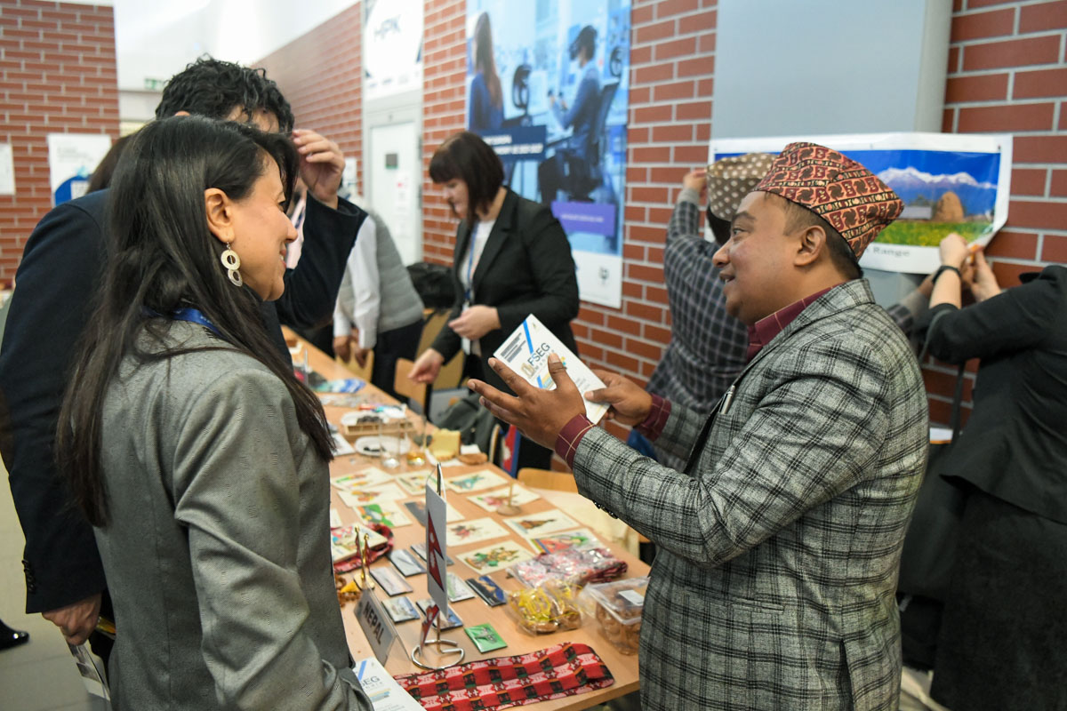 A man from Nepal, wearing the national headwear talking to two people