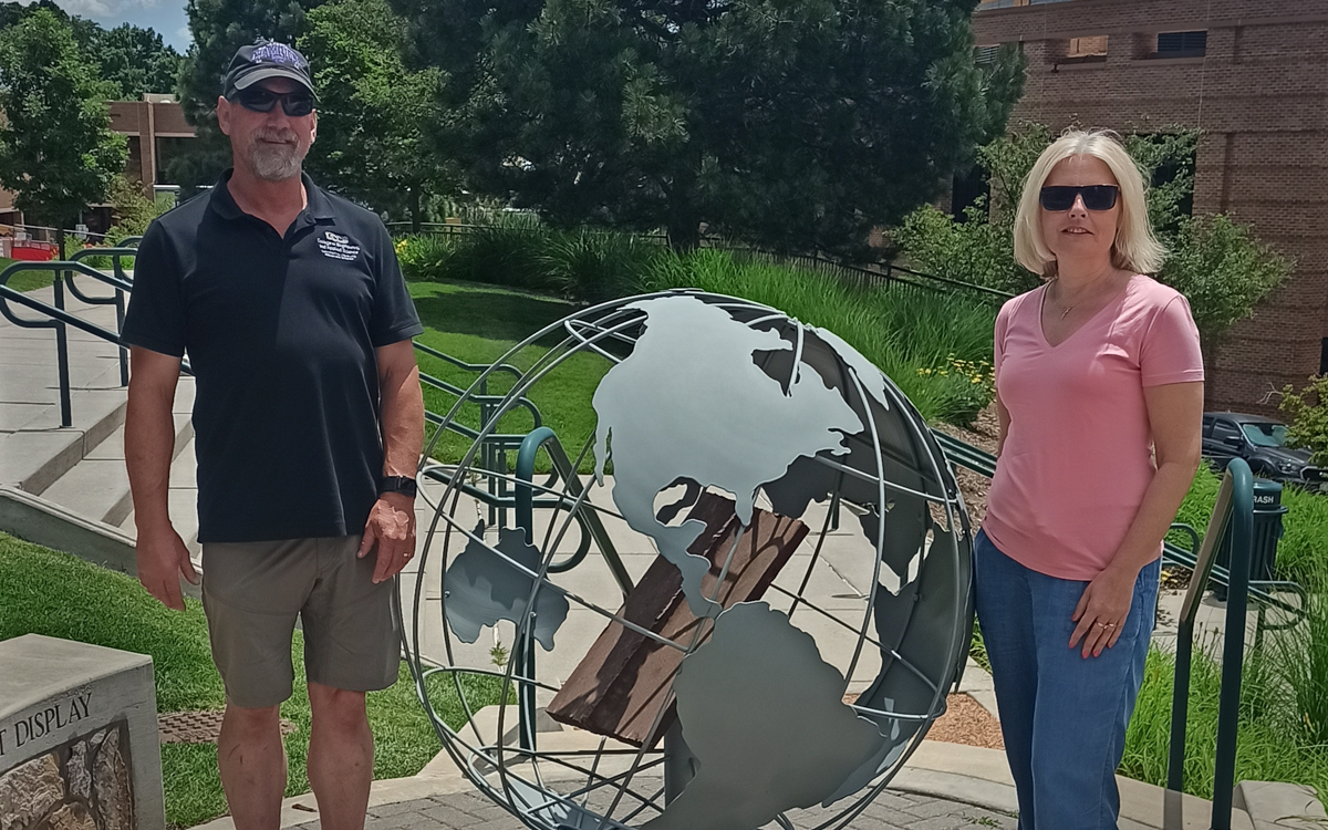 Peter Gorder and Dorota Krawczyk stand on opposite sides of a globe-shaped installation. In the background are stairs, lawns and trees.