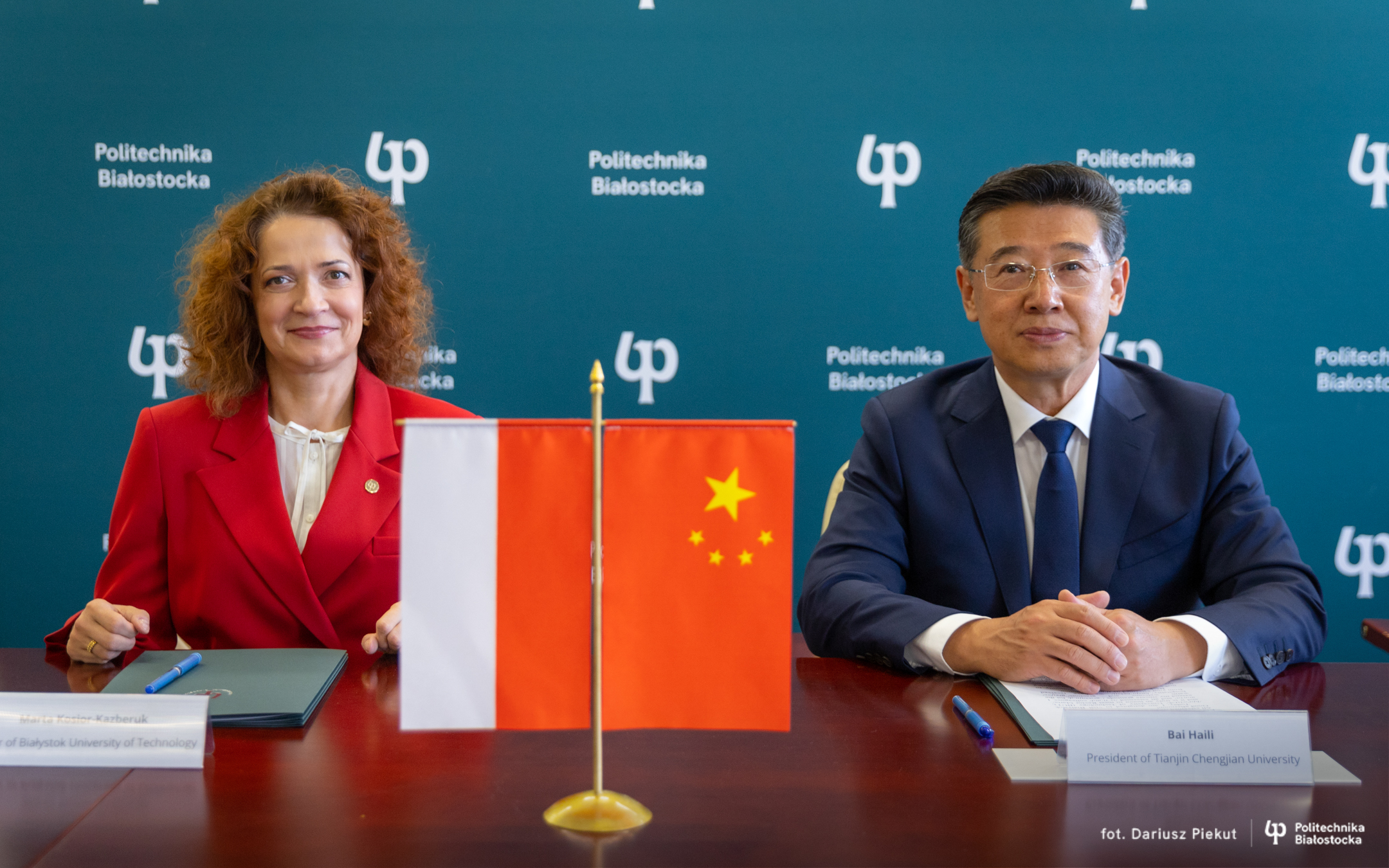 Assoc. Prof. Marta Kosior-Kazberuk, DSc, PhD, Eng, Rector of BUT and Prof. Bai Haili, Rector of Tianjin Chengjian University sit at a table, documents lie in front of them, Polish and Chinese flags are on the table.