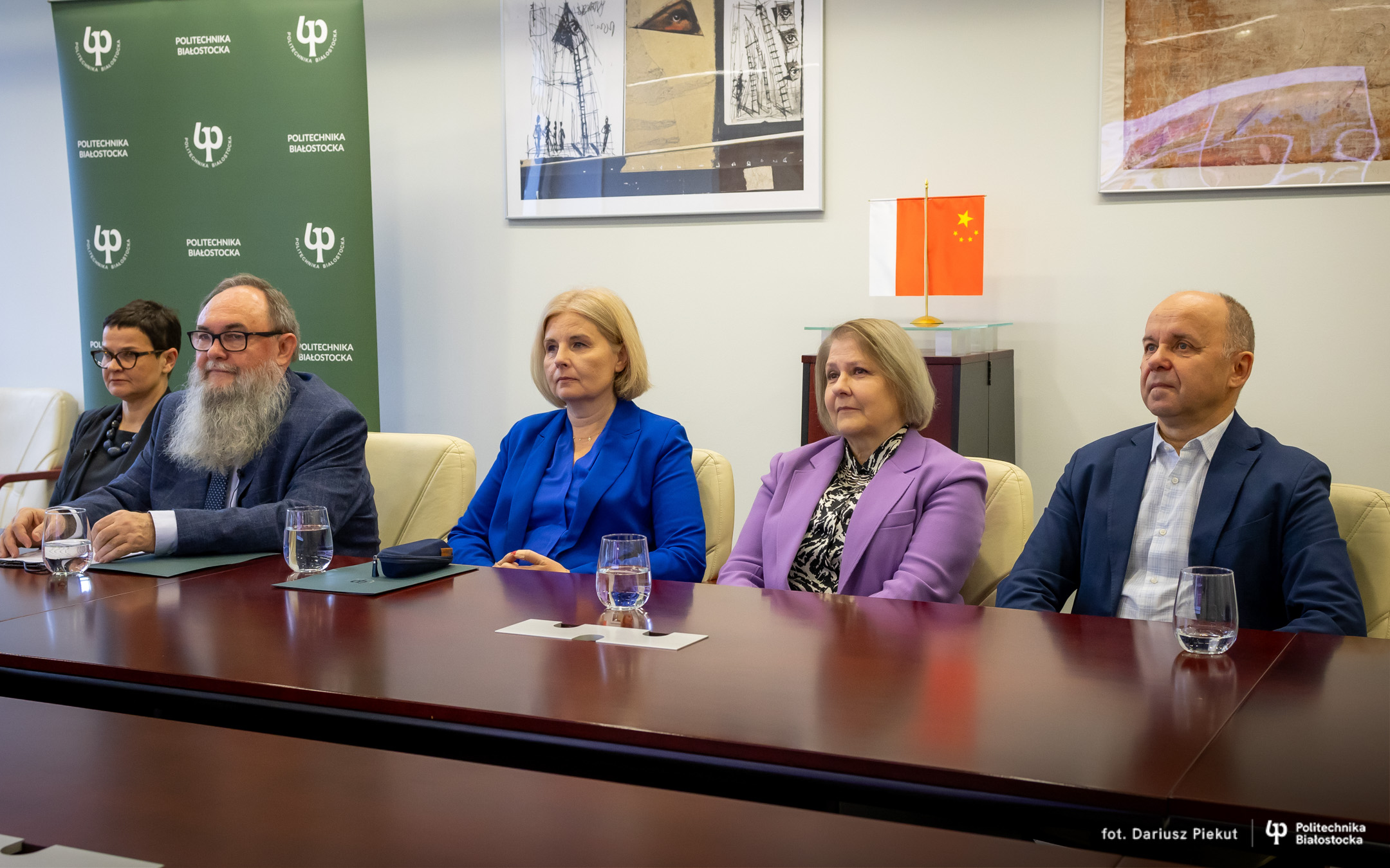 Five people sit at a table; in the background, there are flags of Poland and China