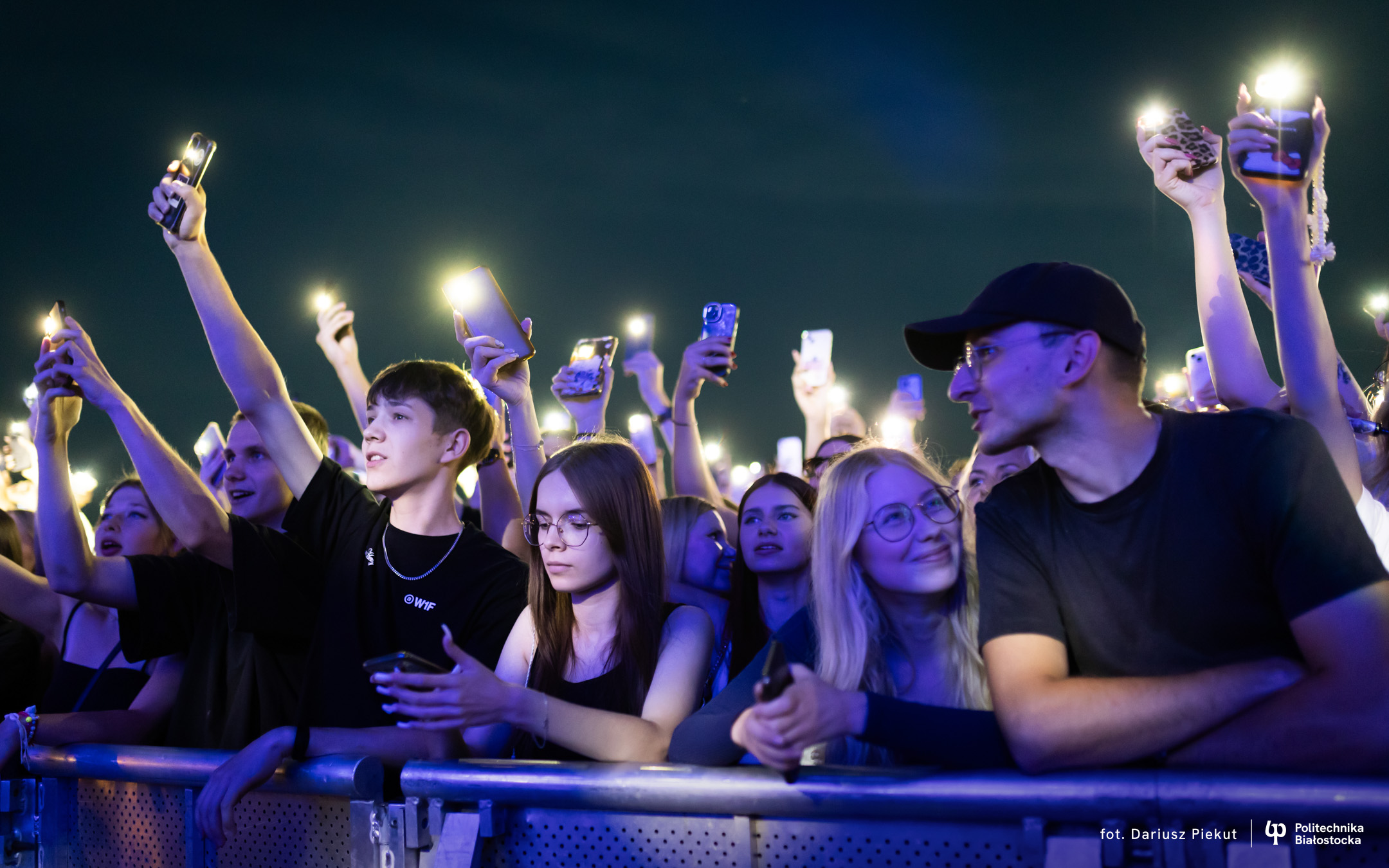 Młodzież przy barierce festiwalowej z zapalonymi smartfonami