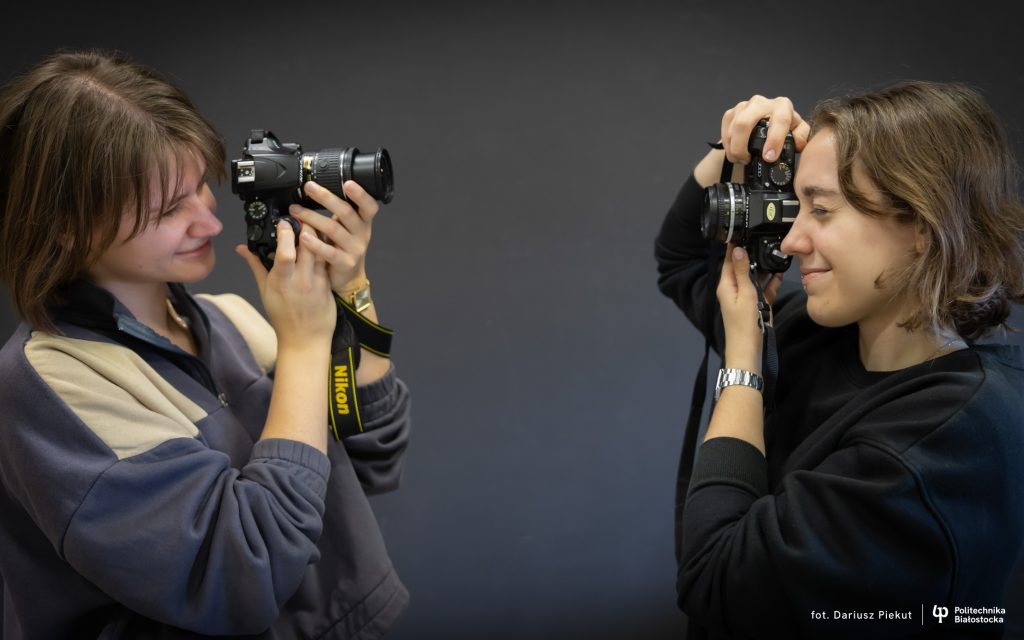 Dwie osoby stoją naprzeciw siebie i robią sobie zdjęcia, trzymając aparaty fotograficzne w studiu z ciemnym tłem