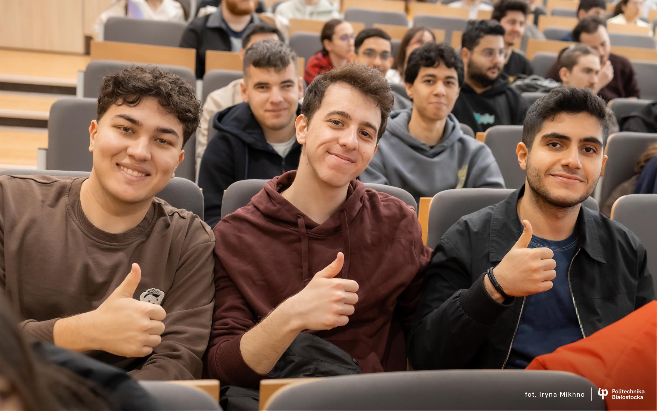 Kilku uśmiechniętych młodych ludzi siedzi na auli