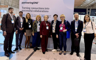 A group of people standing at a trade fair booth in front of a “partneringONE” banner, posing for a group photo during an industry event