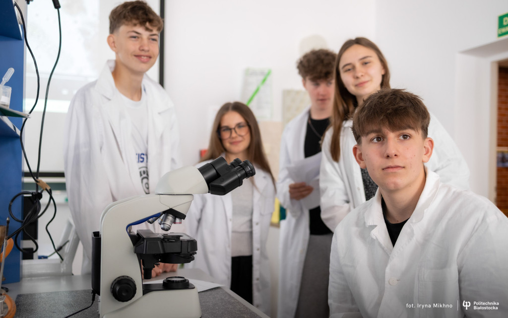pięciu uczniów siedzi w laboratorium, w białych fartuchach