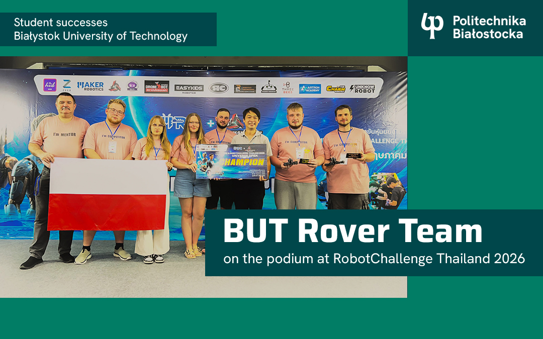 A group of people stand in front of an event backdrop holding the Polish flag and a “Champion” sign, with visible logos and a PB Rover Team banner