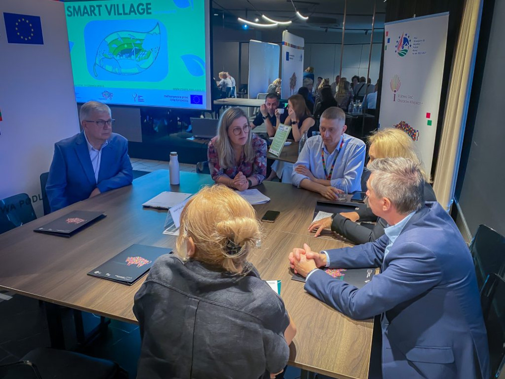 Grupa ludzi wokół stołu, w tle grafika z rzutnia z napisem Smart Village